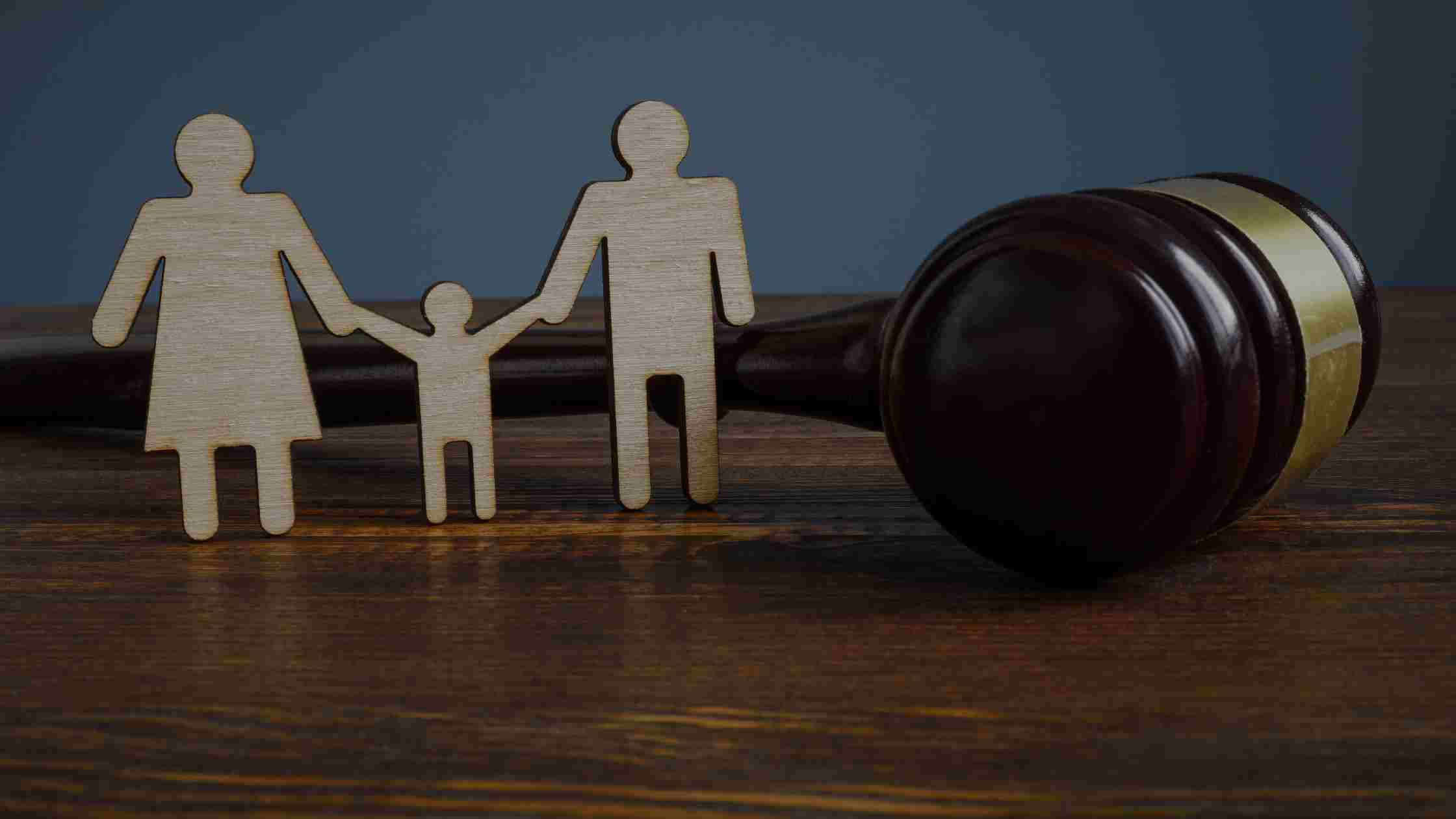 Shows three wooden figures of a family of three next to a gavel on a wooden surface to represent family law.